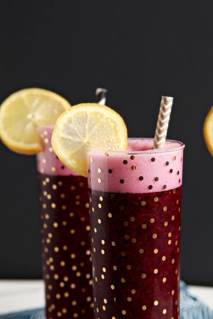 Three glasses of deep purple-colored Spiked Blueberry Lemonade sit together in front of a black background