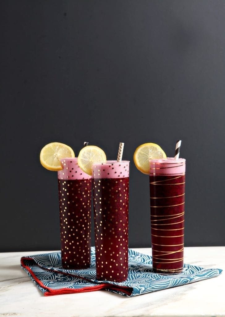 Three glasses of blueberry lemonade vodka with lemon round garnishes on marble