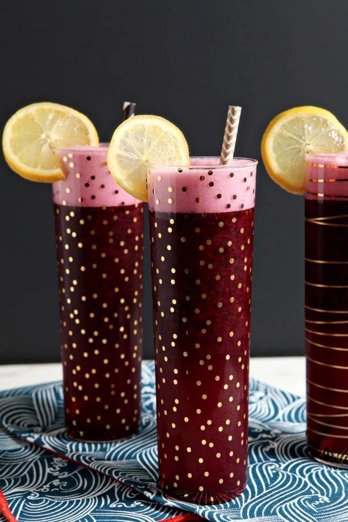 Three champagne glasses of spiked blueberry lemonade with lemon garnishes