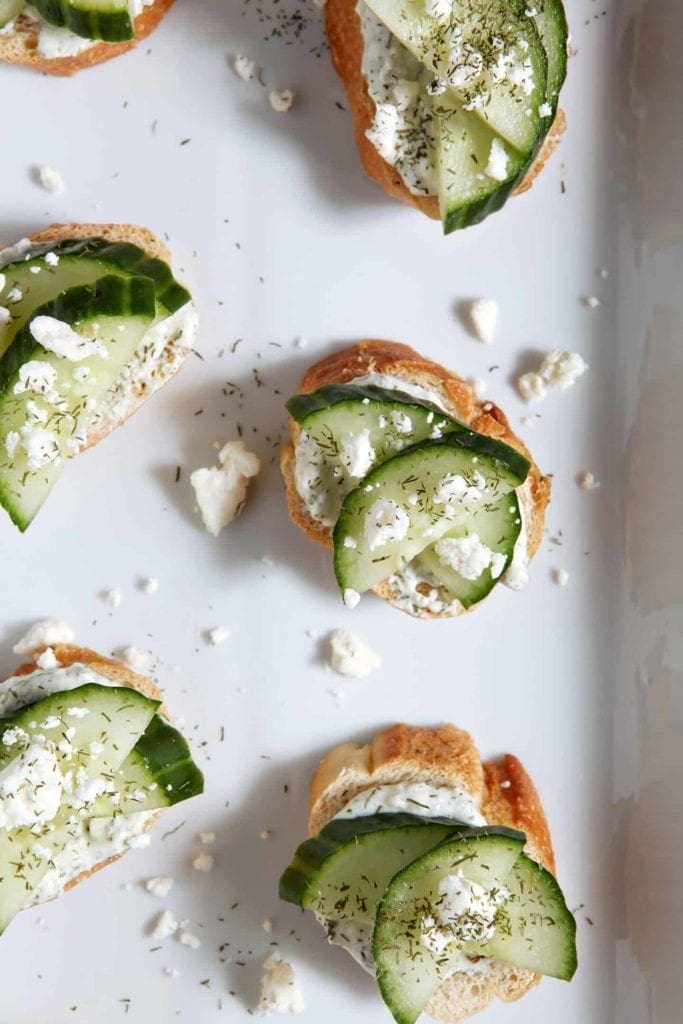 Overhead of Cucumber Bruschetta sitting on a white platter, garnished with additional feta cheese and dill