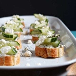 Cucumber Bruschetta, served on a white platter, sits on a wooden background