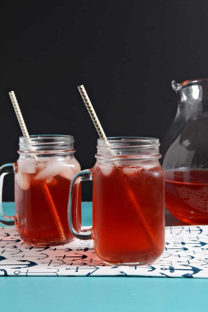 Two iced glasses of Strawberry Sweet Tea sit on a turquoise table with a pitcher