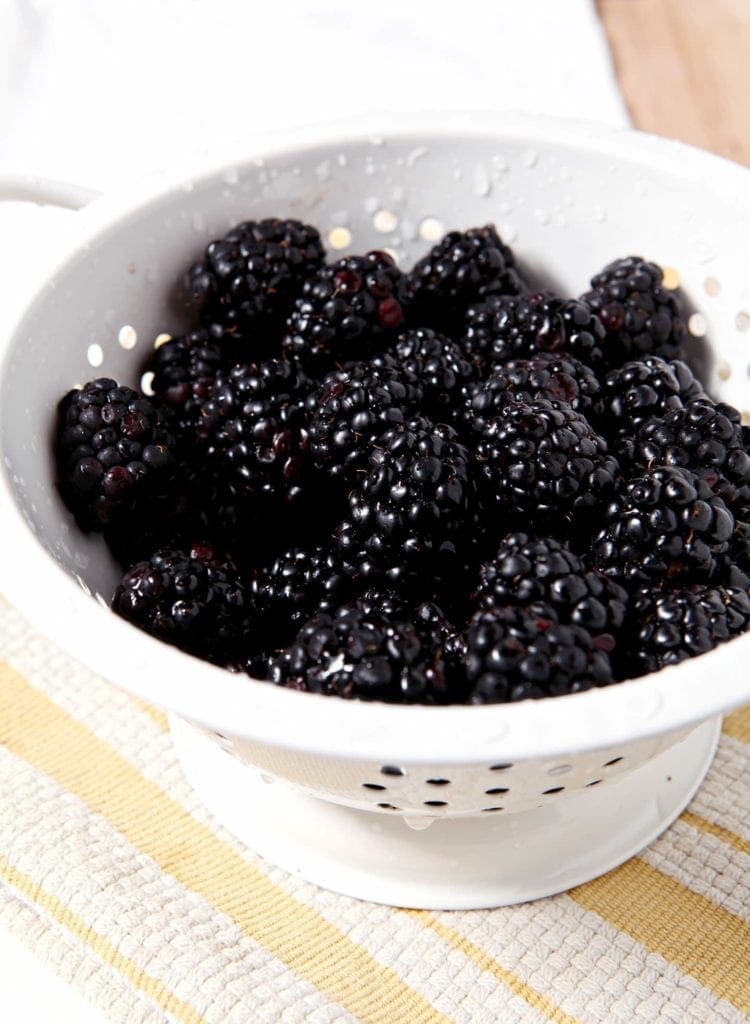 A white colander full of fresh blackberries