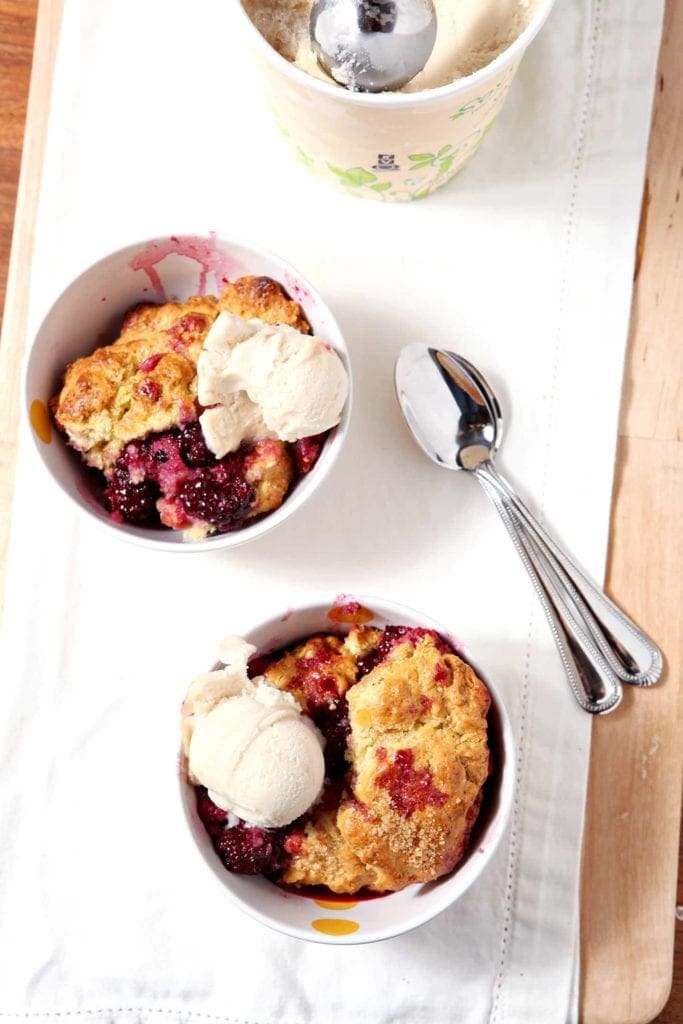 Two bowls of blackberry cobbler with spoons on linens 