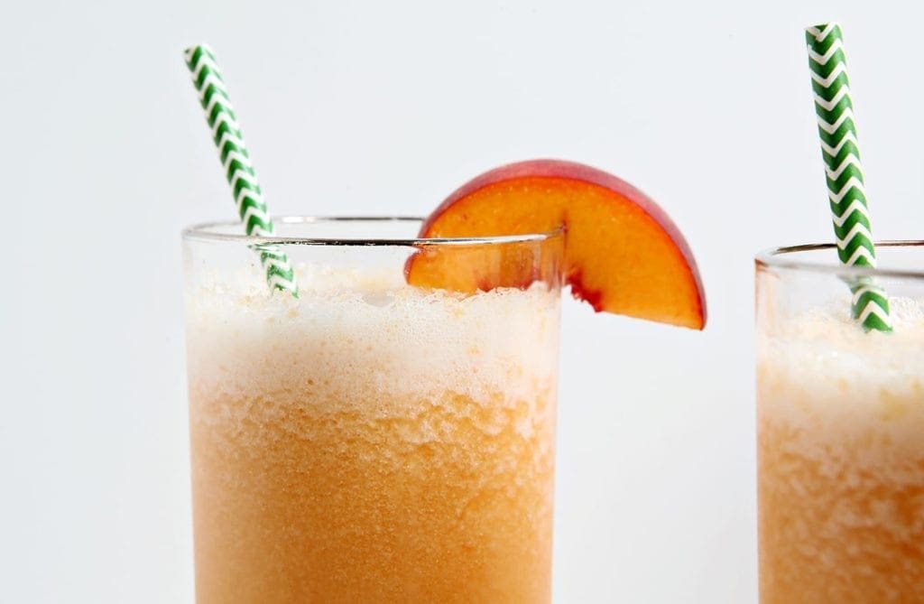 Two highball glasses of peach bourbon slushes with green chevron straws