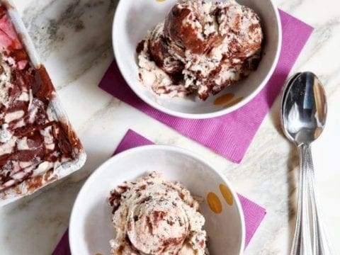 Two bowls filled with scoops of ice cream on purple napkins with spoons