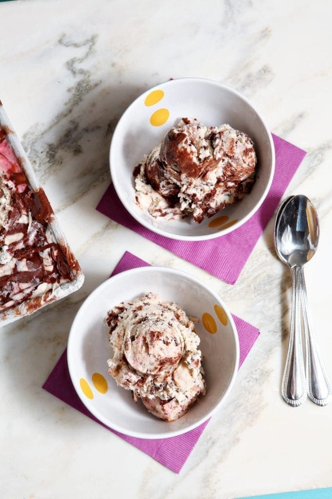 Two bowls filled with scoops of ice cream on purple napkins with spoons 