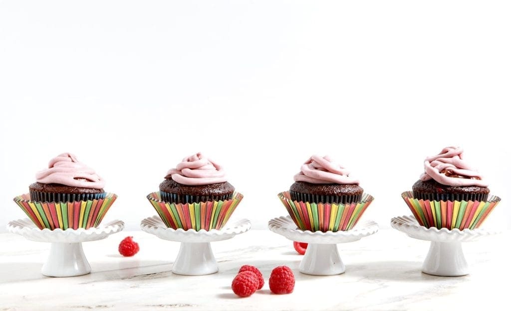 A line of cupcakes in striped wrappers on top of white stands 