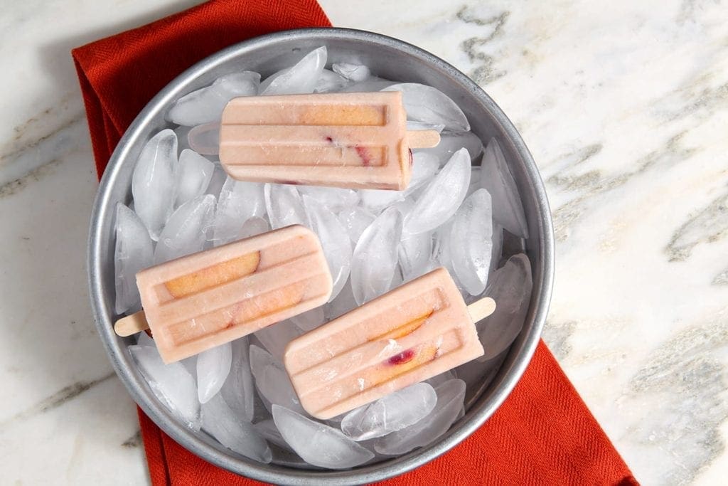 Three popsicles on top of bowl of ice cubes 