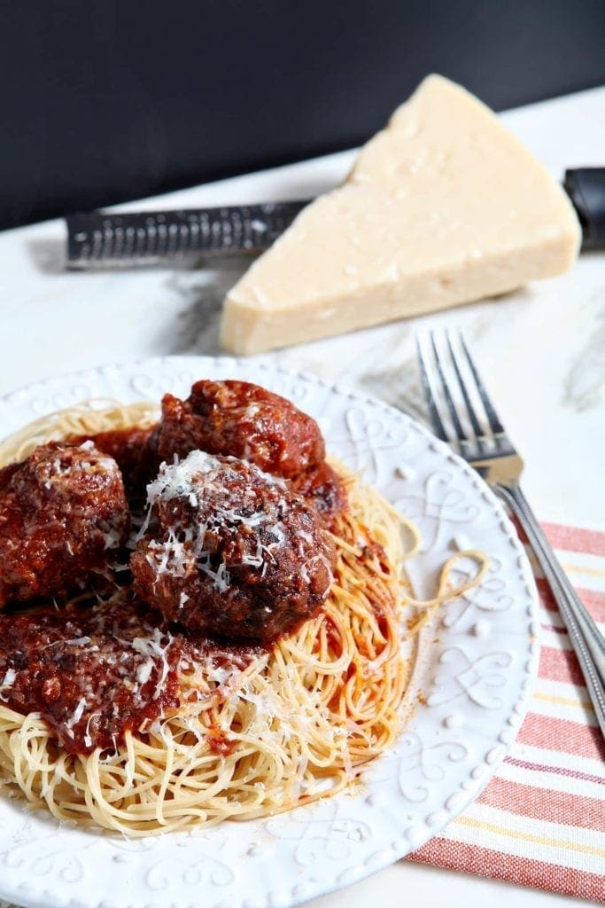 White plate of spaghetti and meatballs with fork and grated cheese 