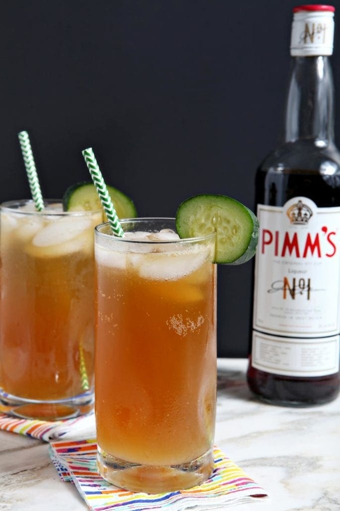 Two Pimm's Cups are served next to a Pimm's No. 1 bottle, garnished with cucumbers