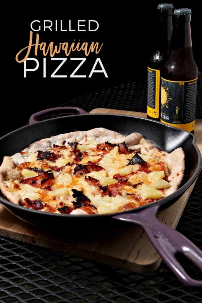 Grilled Hawaiian Pizza, cooked in a cast iron skillet, sits on an outdoor table with beers in the background before eating