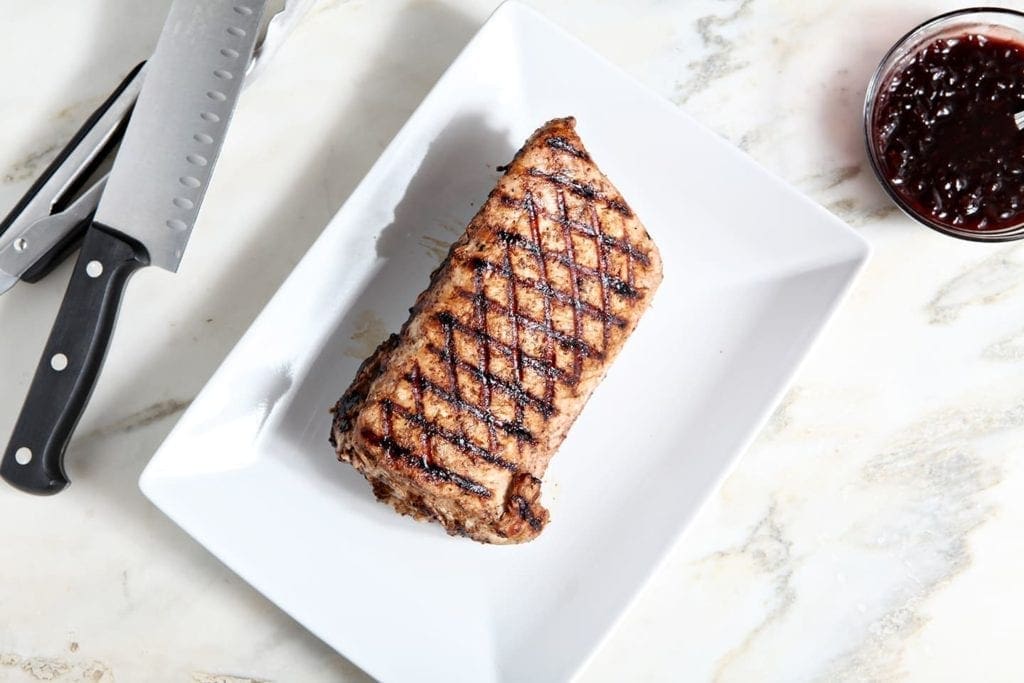 Slab of grilled pork tenderloin on white serving platter 