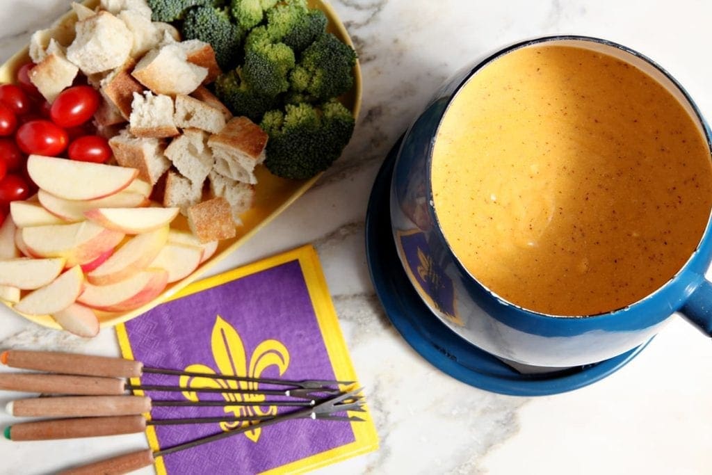 A bowl of fondue with party platter, napkins and dipping utensils 