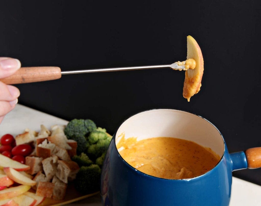 Apple slice dipped in bowl of spicy cheddar fondue 