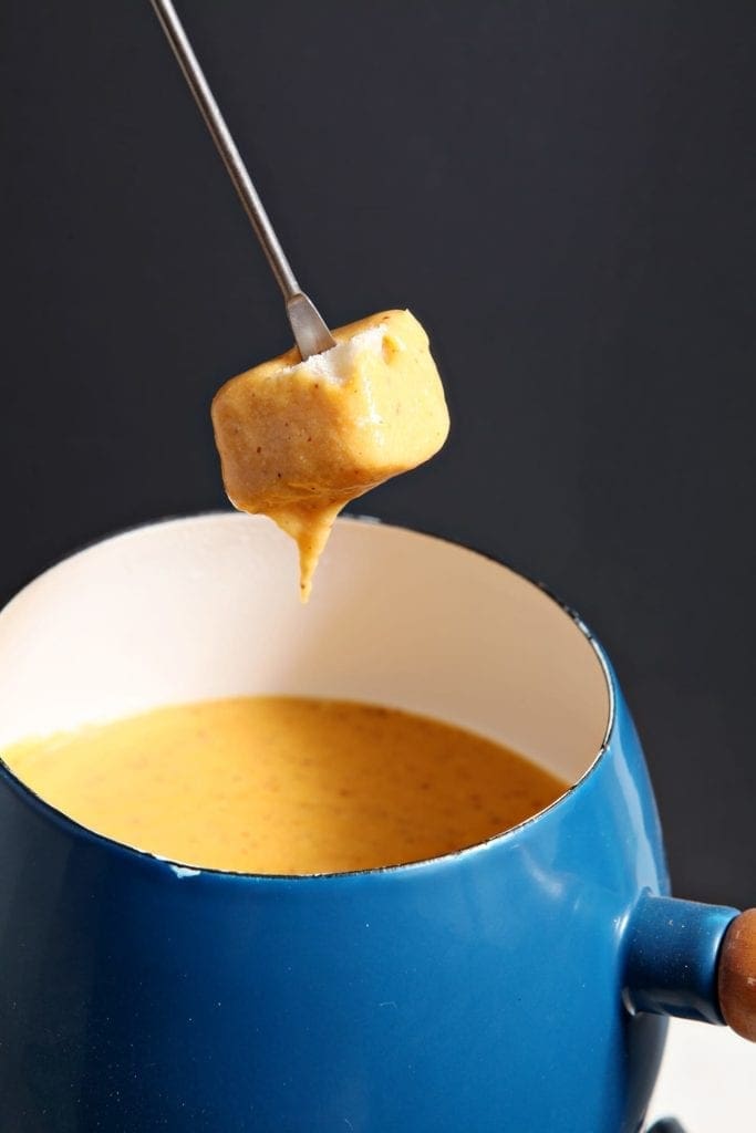 Food dipping into blue bowl of spicy cheddar fondue 