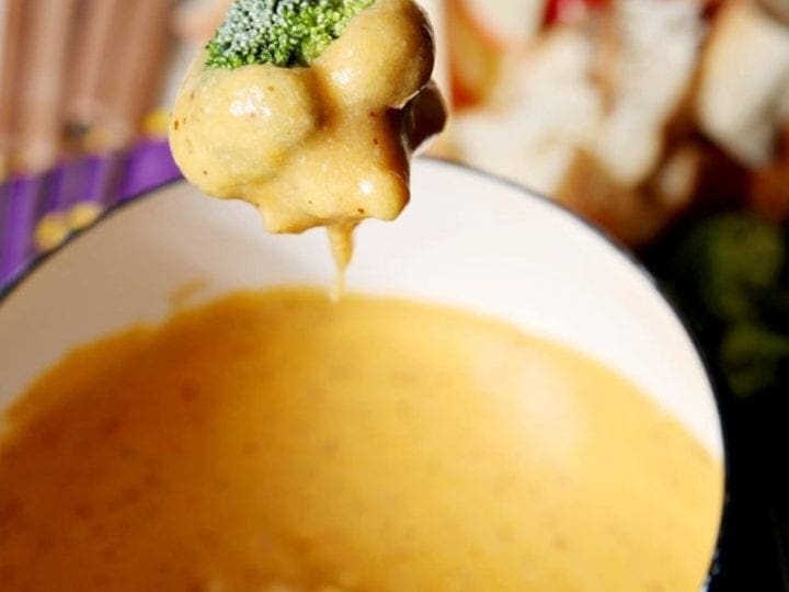 A piece of broccoli being dipped in bowl of fondue