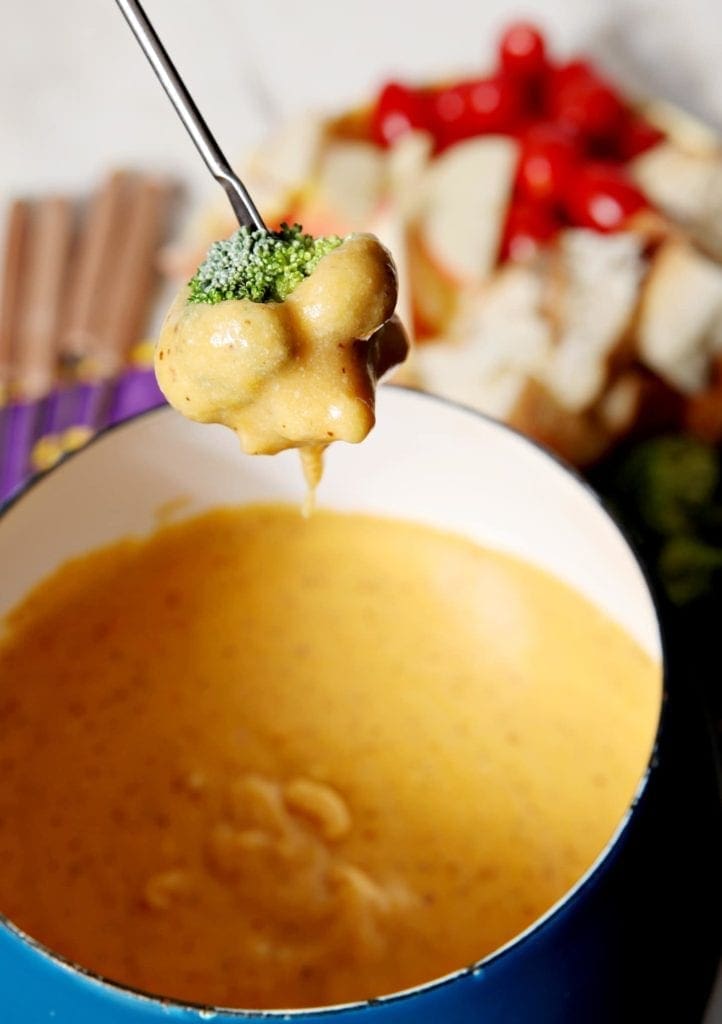 A piece of broccoli being dipped in bowl of fondue 