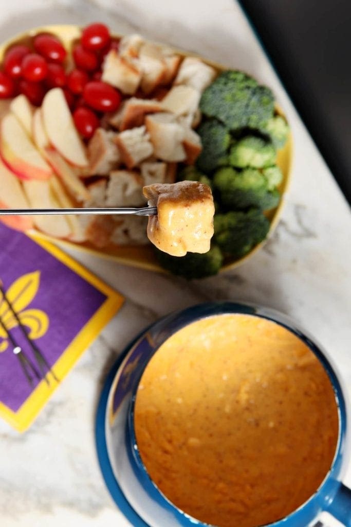 Overhead view of food dipped in bowl of fondue next to party food platter 