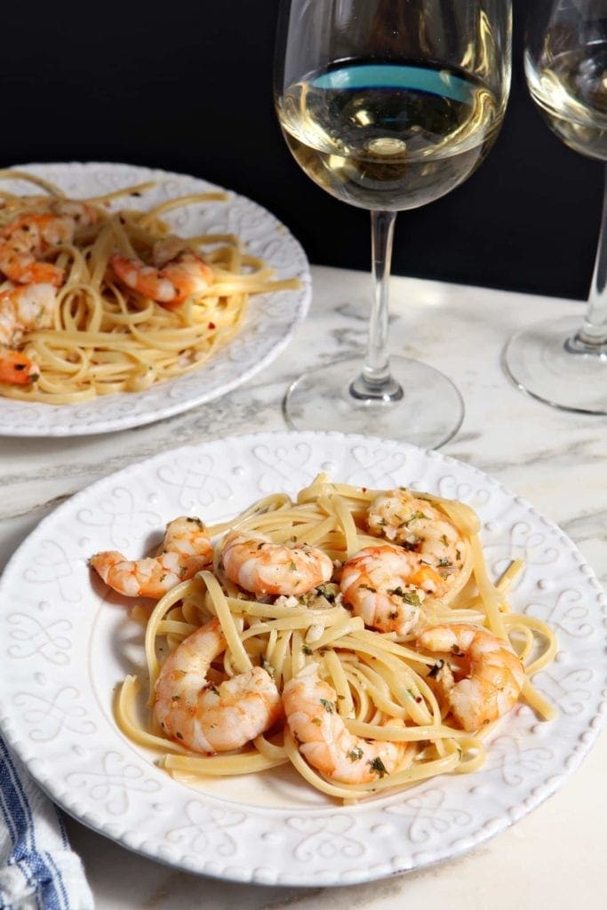 Two plates of Lemon Shrimp Pasta are served with white wine