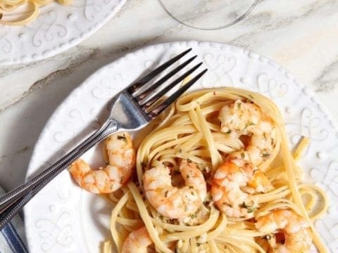 Lemon Shrimp Pasta on a white plate with a fork on marble with a glass of wine
