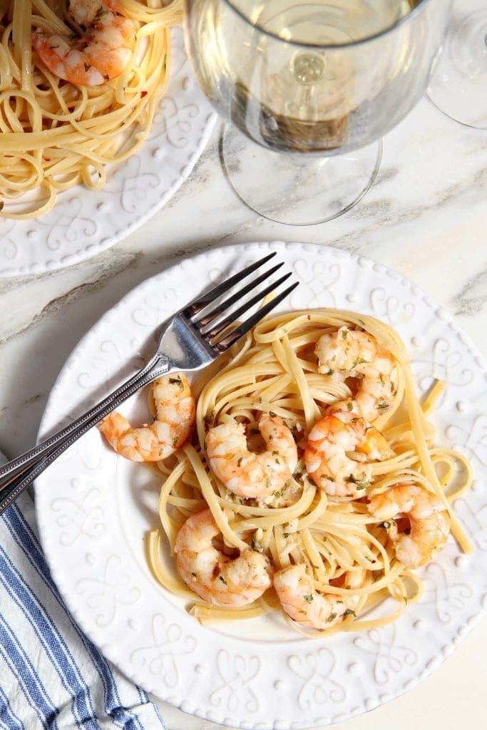 Lemon Shrimp Pasta on a white plate with a fork on marble with a glass of wine