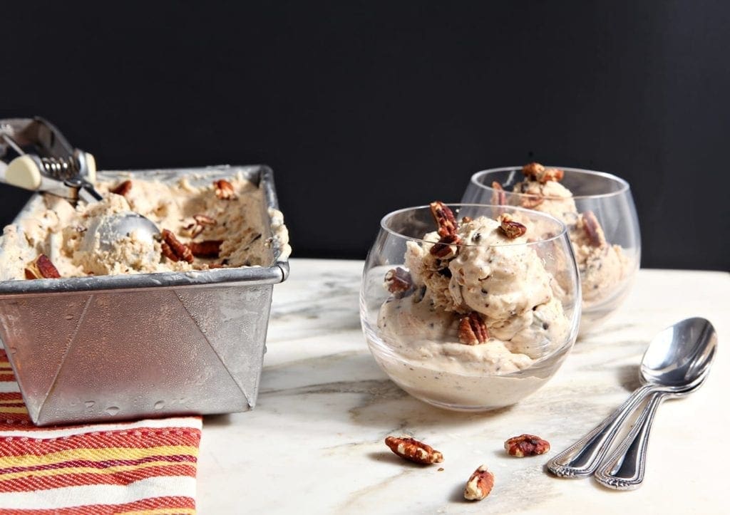 No churn ice cream scoops in cups on marble with pecans and spoons