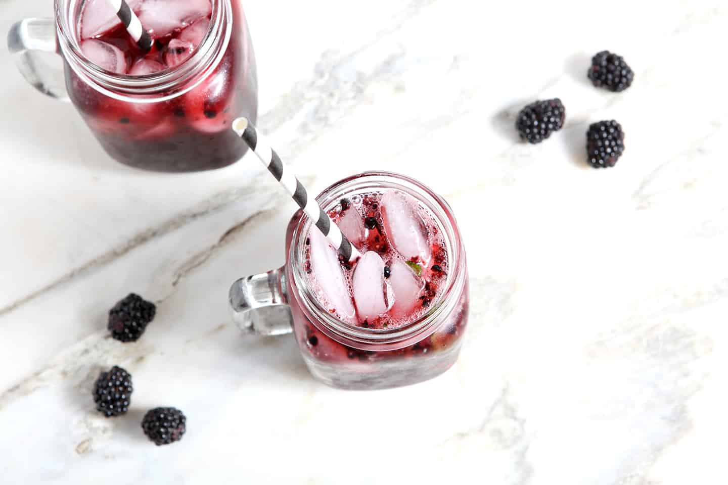 Overhead image of two Blackberry Mint Spritzers, sitting on a marble counter with fresh blackberries surrounding the drinks