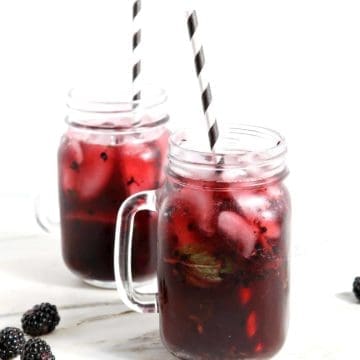 Two Blackberry Mint Spritzer sitting on a marble counter, iced and ready for drinking