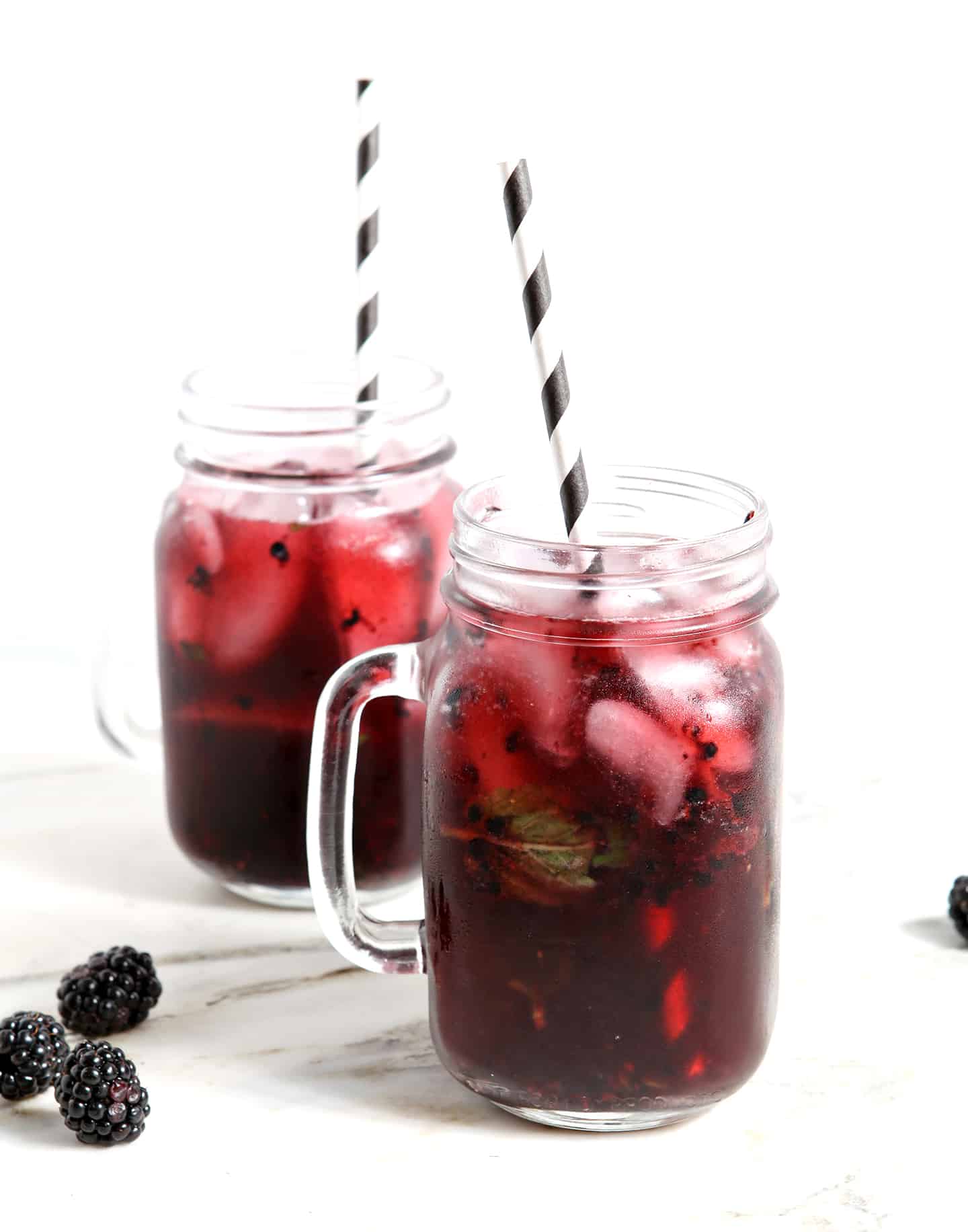 Two Blackberry Mint Spritzer sitting on a marble counter, iced and ready for drinking