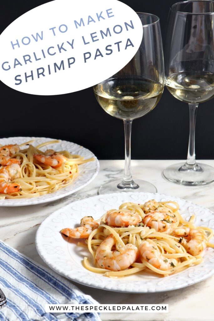 Two white plates hold Lemon Shrimp Pasta on marble with two forks and two glasses of white wine and the text 'how to make garlicy lemon shrimp pasta.'