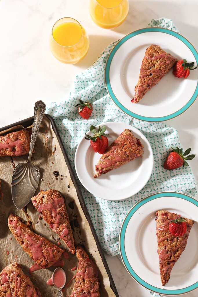 Three plates hold strawberry scones next to a baking sheet with more scones on it