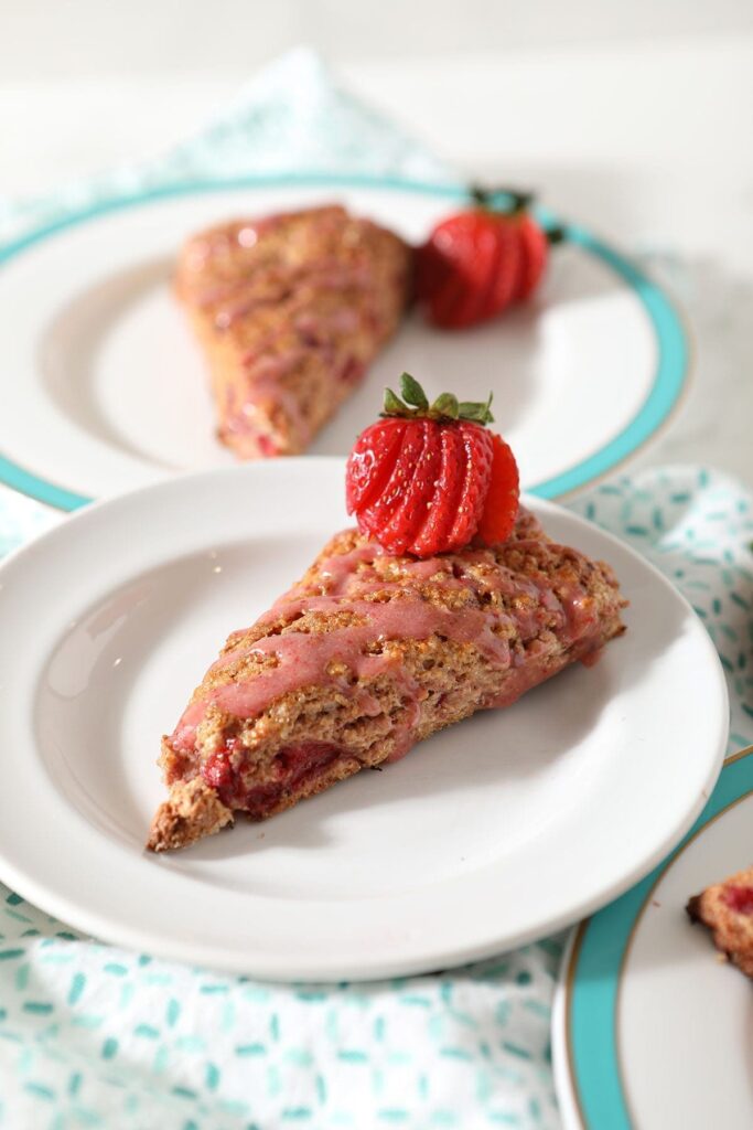 Close up of a Strawberry Scone on a white plate next to two other plates on a turquoise patterned towel