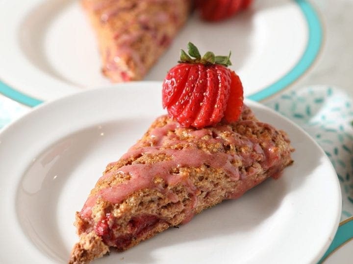 Close up of a Strawberry Scone on a white plate next to two other plates on a turquoise patterned towel