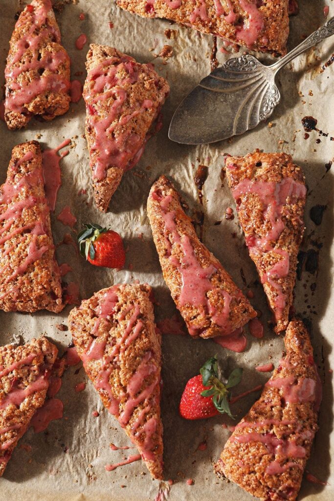 A baking sheet holds various glazed Strawberry Scones with fresh strawberries on it