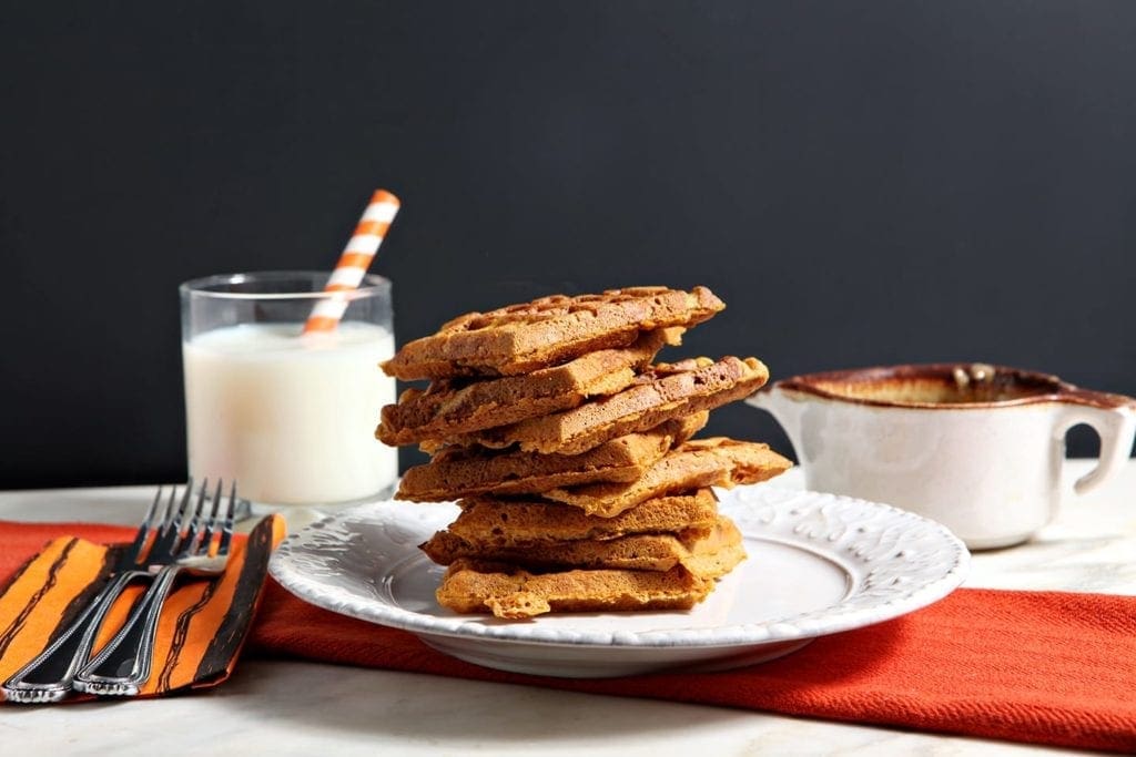 A stack of sliced pumpkin waffles on white plate with a glass of milk 