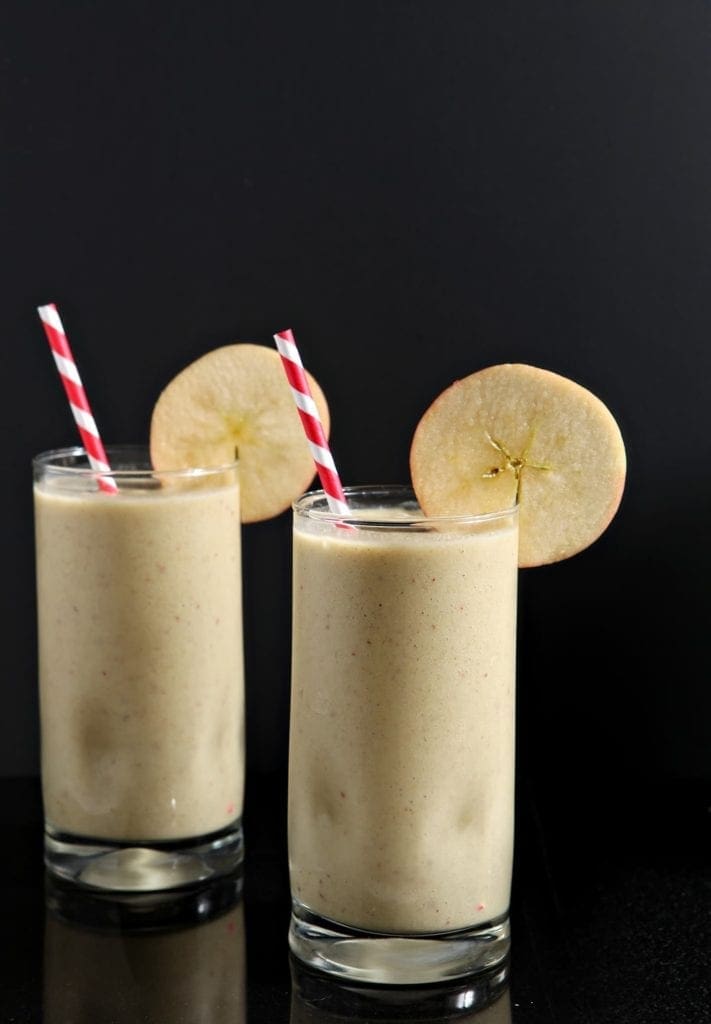 Two glasses of smoothie with straws and apple slice garnish 