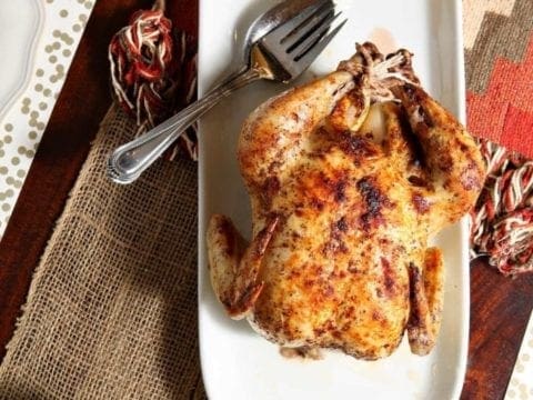 White platter of whole roasted chicken on linens