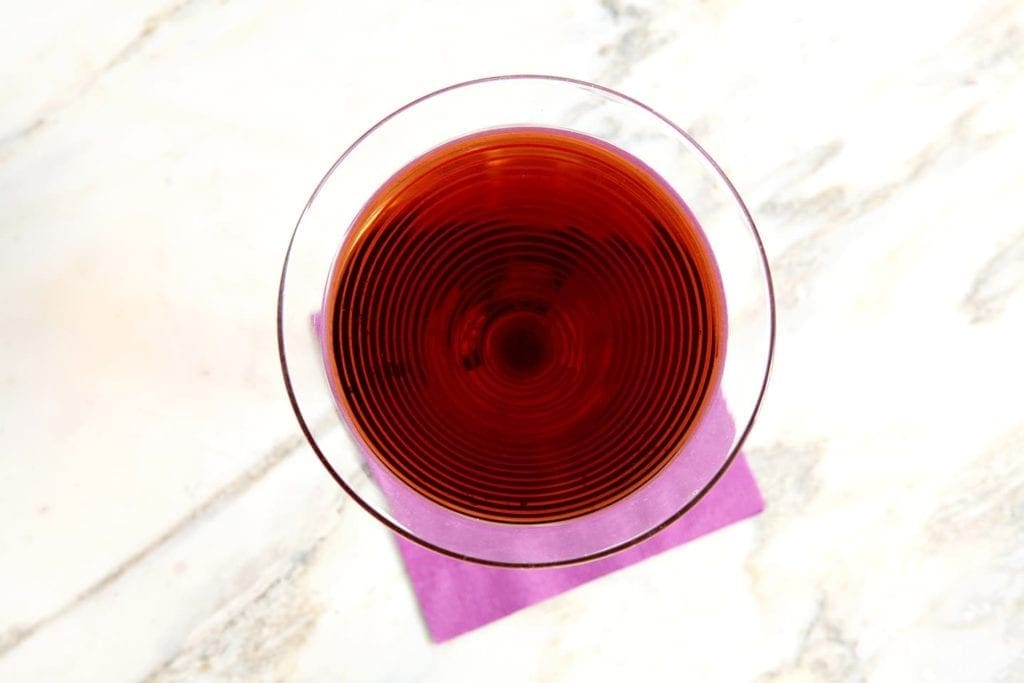 Overhead view of beverage in cocktail glass on purple napkin 