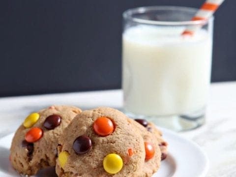 Several Reese's Pieces Peanut Butter Cookies on white plate with glass of milk