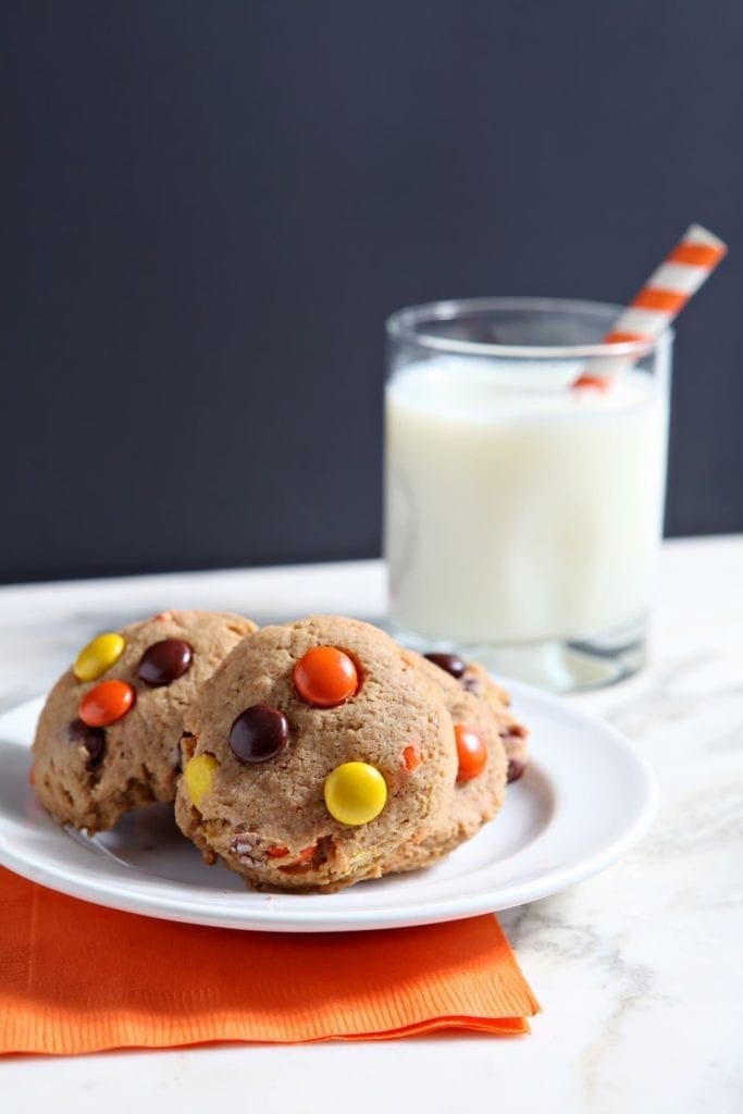 Several Reese's Pieces Peanut Butter Cookies sit on a white plate with a glass of milk