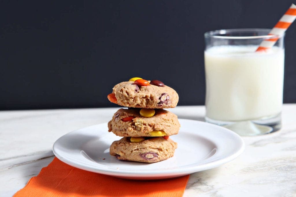 Three cookies stacked on white plate with glass of milk 