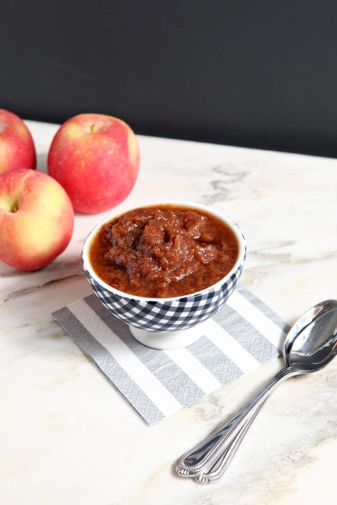 Overhead view of applesauce in bowl next to 3 red apples and spoon 