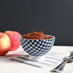 A bowl of slow cooker applesauce in front of 2 red apples