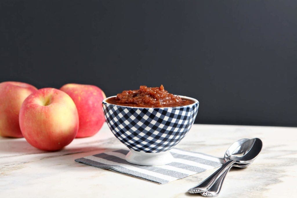 A bowl of slow cooker applesauce in front of 2 red apples 