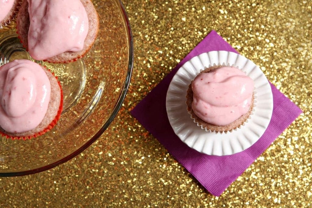 Overhead of a strawberry cupcakes with strawberry cream cheese frosting on a white cake stand