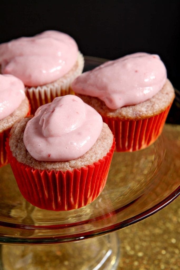 Close up of strawberry cupcakes on a cake stand sitting on a golden tray