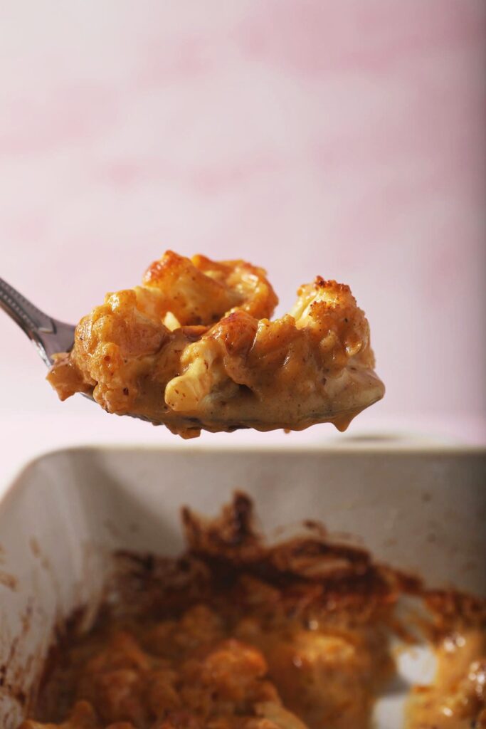 A spoon holds a serving of cheesy cauliflower bake over a casserole dish