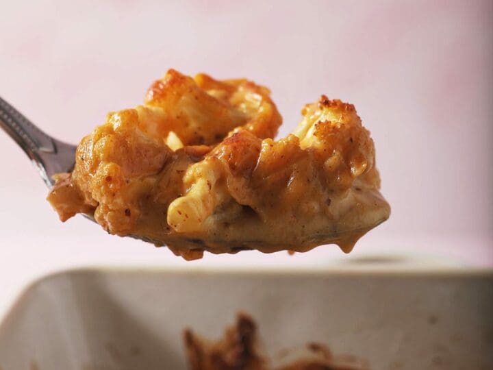 A spoon holds a serving of cheesy cauliflower bake over a casserole dish