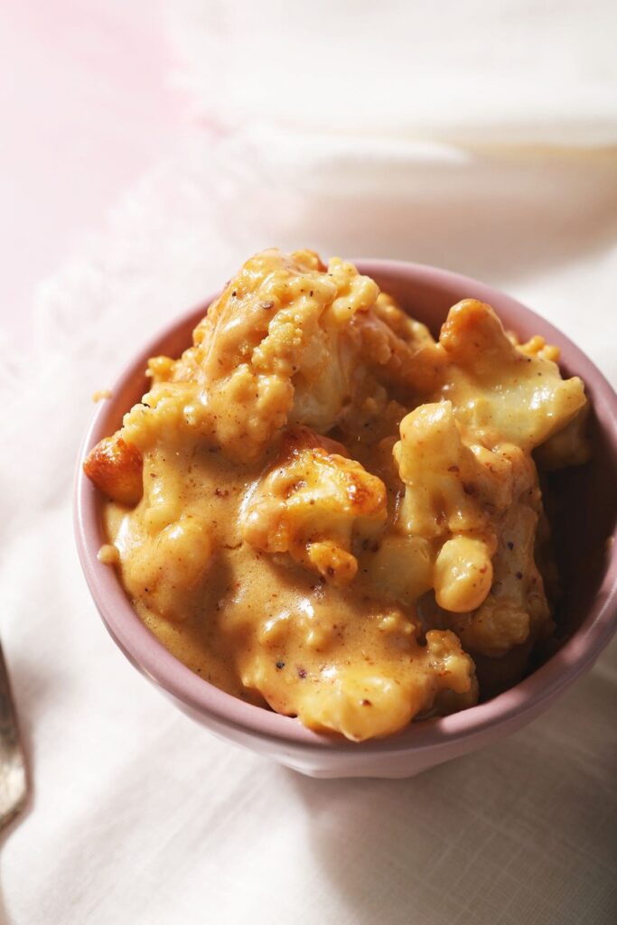 A pink bowl holds a serving of cheesy cauliflower bake in a white napkin